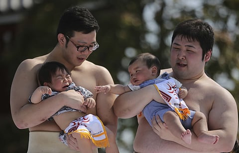 அழும் குழந்தைகள் போட்டியில் பங்கேற்ற குழந்தைகளை ஏந்தியுள்ள சுமோ வீரர்கள் - கோப்பிலிருந்து