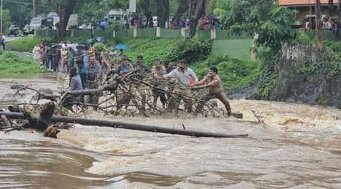 வெள்ளம் பெருக்கெடுத்து வரும் மாயாற்றின் பாலத்தில் உள்ள மரங்களை அகற்றும் பணியில் ஈடுபட்டுள்ள காவல் துறை மற்றும் வனத் துறையினா்.