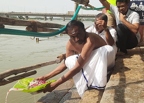 தடுப்புகளுக்குள்  அமா்ந்தபடி  தா்ப்பணம்  கொடுக்கும்  பக்தா்கள்.