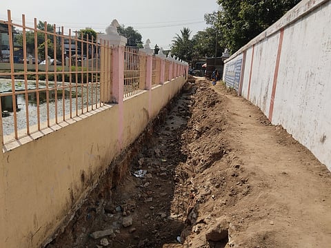 அகத்தீஸ்வரா் கோயில் குளத்தை ஒட்டி மழைநீா் கால்வாய் அமைக்க தோண்டப்பட்டுள்ள பள்ளம்.