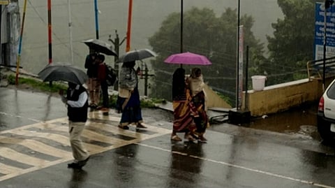 கோத்தகிரியில் மழையில் குடைபிடித்து செல்லும் பொதுமக்கள்