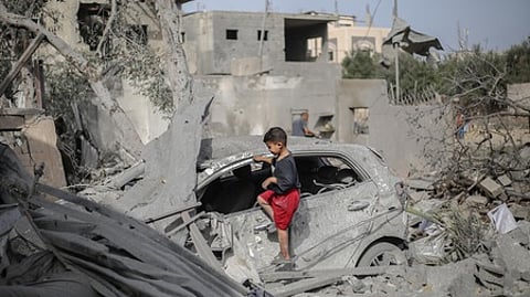 இஸ்ரேல் தாக்குதலால் உருக்குலைந்த காரில் விளையாடும் சிறுவன்.