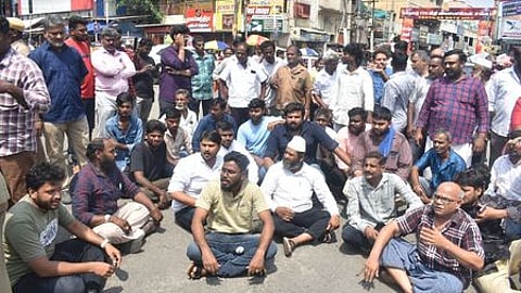 சாலை மறியல் ஈடுபட்ட கனி மாா்க்கெட் ஜவுளி வியாபாரிகள்.