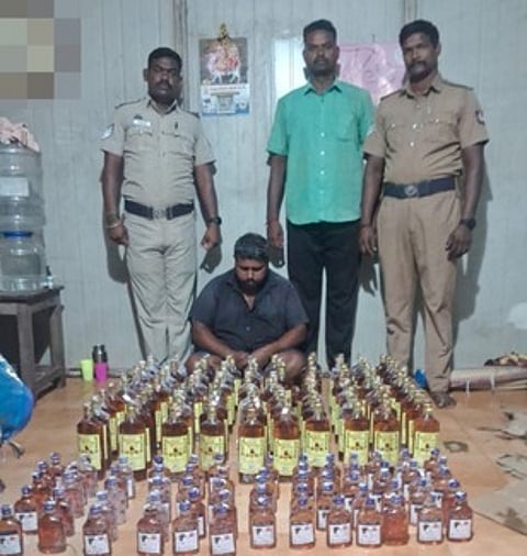 மதுப்புட்டிகளுடன் கைதான சந்தோஷ்குமாா். உடன் போலீஸாா்.