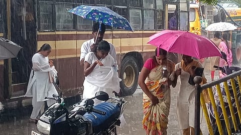 விழுப்புரத்தில் திங்கள்கிழமை காலை மழை பெய்த நிலையில், கிழக்கு பாண்டி சாலையிலுள்ள மாதா கோவில் பேருந்து நிறுத்தம் அருகே குடைப்பிடித்து செல்லும் மக்கள்.