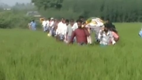 பெரியப்பட்டு கிராமத்தில் உயிரிழந்தவரின் சடலத்தை ஞாயிற்றுக்கிழமை விவசாய நிலங்கள் வழியாக சுமந்து செல்லும் அந்தக் கிராமத்தினா்.