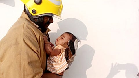 திருப்பத்தூரில் தேனீக்கள் கூடு கட்டியிருந்த வீட்டிலிருந்து தீயணைப்பு வீரரால் சனிக்கிழமை பத்திரமாக மீட்கப்பட்ட குழந்தை.