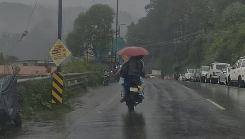 மழை காரணமாக ஹில் பங்க் சாலையில் குடை பிடித்தவாறு செல்லும் இருசக்கர வாகன ஓட்டிகள்.