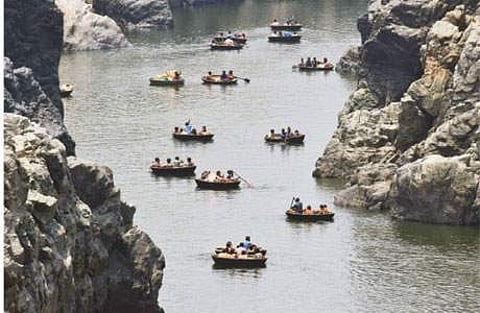 அருவியில் பரிசல் சவாரி செல்லும் சுற்றுலாப் பயணிகள்.