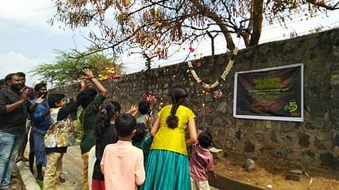 தங்களை காத்தற்காக பட்டுபோன வேப்ப மரத்திற்கு  மலர்தூவி நன்றி தெரிவிக்கும் குழந்தைகள்.