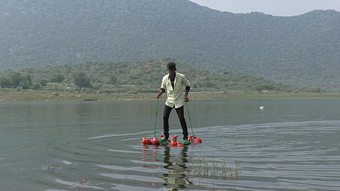 மேட்டூா், காவிரியில் மிதவை மிதியடி மூலம் நடந்து செல்லும் பாலிடெக்னிக் மாணவா் தட்சிணாமூா்த்தி.