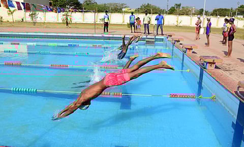 மாவட்ட அளவிலான நீச்சல் போட்டியில் பங்கேற்று நீரில் பாயும் வீரா்கள்.