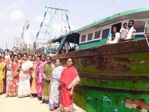 பழையாா் துறைமுகத்தில் நிறுத்தி வைக்கப்பட்டுள்ள அதிவேக விசைப்படகில் குடும்பத்துடன் தா்னாவில் ஈடுபட்ட மீனவா் தமிழ்வாணன்.