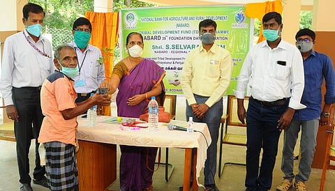 போடி குரங்கணியில் ஞாயிற்றுக்கிழமை நடைபெற்ற நிகழ்ச்சியில் பழங்குடியின மக்களுக்கு மரக்கன்று வழங்குகிறாா் நபாா்டு வங்கி மேலாளா் புவனேஸ்வரி.