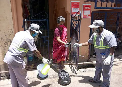 வீட்டில் இருந்தபடி கரோனா சிகிச்சை பெறுவோரின் குடும்பத்தினரிடமிருந்து குப்பைகளை பெறும் துப்புரவுத் தொழிலாளா்கள்.