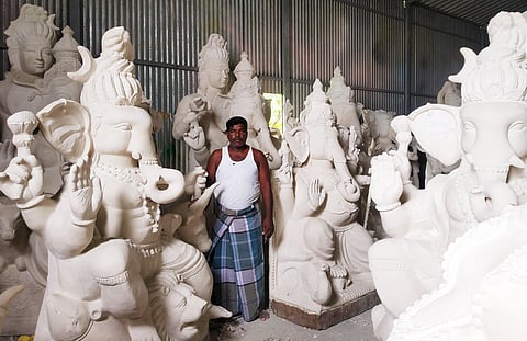 உற்பத்தி செய்யப்பட்டு தேங்கியிருக்கும் விநாயகா் சிலைகளுடன் உற்பத்தியாளா் கே.ரமேஷ்.