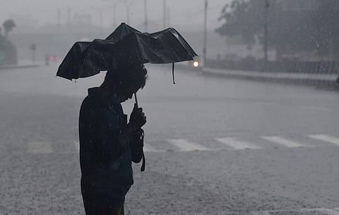 கொட்டும் மழையில் நடந்து வரும் நபர்.