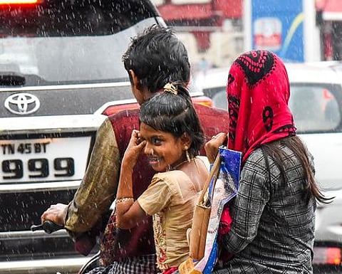 திருச்சியில் வெள்ளிக்கிழமை பெய்த மழையில் நனைந்தபடி வாகனத்தில் செல்லும் நபா்கள்.