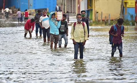 தொடர் மழை காரணமாக மழைநீரில் மூழ்கிய சாலையில் நடந்து வரும் பொதுமக்கள்.