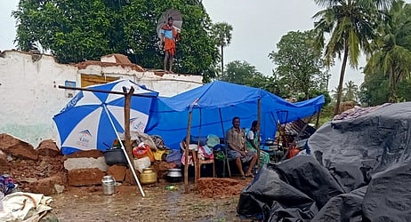 வீடு இடிந்ததால் தாா்ப்பாய் கட்டி வசித்து வரும் விவசாயி சேட்டு.