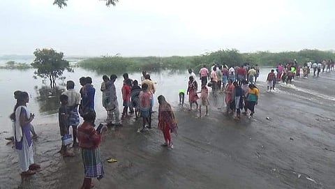 தூசூர் ஏரி நிரம்பி சாலையில் வழிந்தோடும் தண்ணீரை ஆர்வமுடன் பார்த்து ரசிக்கும் அந்த பகுதி மக்கள்.