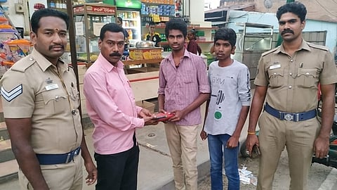 கம்பத்தில் சாலையில் கிடந்த பணம் மற்றும் செல்லிடப்பேசியை போலீஸாரிடம் சனிக்கிழமை ஒப்படைத்த மாணவா் முத்துக்குமாா்.