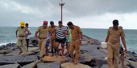 கடற்கரையில் கருங்கற்கலுக்கு இடையே சிக்கியவரை மீட்டு வரும் தீயணைப்புத் துறையினா் மற்றும் போலீஸாா்.