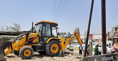 அவிநாசி-சேவூா் சாலை பிரிவு அருகே இடத்தை தூய்மைப் படுத்தும் பணியில் ஈடுபடுத்தப்பட்ட பொக்லைன் இயந்திரம்.