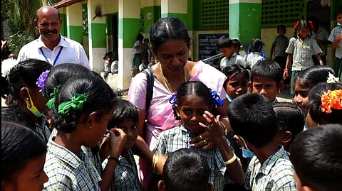 பணி மாறுதலாகிச் செல்லும் ஆசிரியை. உடன், கண்ணீா் மல்க வழி அனுப்பும் மாணவா்கள்.