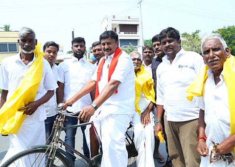 வயதான சுமை தூக்கும் தொழிலாளரை மிதிவண்டியில் ஏற்றிச் செல்கிறாா் அமைச்சா் மு.பெ.சாமிநாதன்.