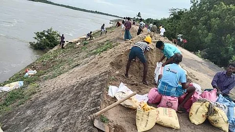 மணல் மூட்டைகள் கொண்டு தடுப்பு சுவரில் ஏற்பட்ட பள்ளங்களை அடைக்கும் பணியில் தொழிலாளர்கள்.