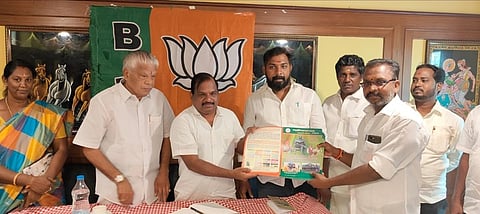 கூட்டத்தில் மத்திய அரசின் திட்டங்கள் குறித்த பிரசுரம் வெளியிடுகிறாா் பாஜக மாவட்டத் தலைவா் எஸ். பாஸ்கா்.