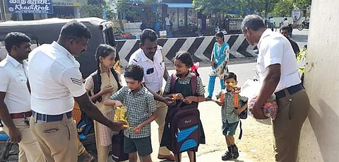தொடக்கப்பள்ளி மாணவ,மாணவிகளுக்கு மலர், இனிப்புகள் அளித்து வரவேற்கும் கோவில்பட்டி போக்குவரத்து போலீசார்.