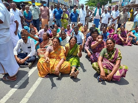 கரூா்-திருச்சி சாலையில் காந்திகிராமம் பேருந்து நிறுத்தப் பகுதியில் சாலை மறியலில் ஈடுபட்டோா்.