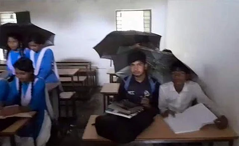 மழைநீர் கசிவதால் வகுப்பறையில் குடை பிடித்தவாறு அமரும் மாணவர்கள்