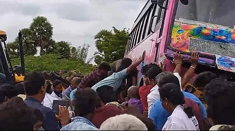 பேருந்துக்கு அடியில் சிக்கி உள்ள காரை பேருந்தை சாய்த்து காரில் இருந்தவர்கள் மீட்டனர்.
