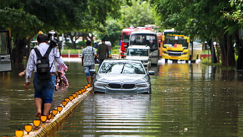 தில்லியில் கனமழைக்கு பிறகு தண்ணீர் தேங்கிய சாலையின் நடுவே உள்ள டிவைடர் மேல் நடந்து செல்லும் பொதுமக்கள்.