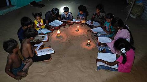 மின்சாரமின்றி விளக்கு வெளிச்சத்தில் படிக்கும் மாணவா்கள்
