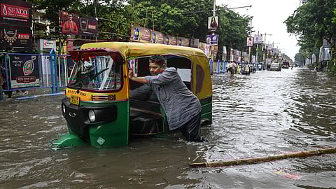 கொல்கத்தாவில் பெய்த கனமழைக்குப் பிறகு வெள்ளம் சூழ்ந்த சாலையில் தனது பழுதடைந்த ஆட்டோ ரிக்‌ஷாவைத் தள்ளிச் செல்லும் நபர் ஒருவர்.