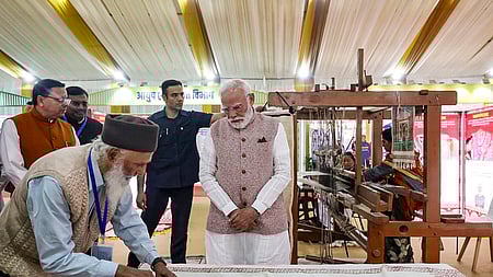 உத்தரகண்ட் மாநிலம் உருவான தினத்தையொட்டி தலைநகா் டேராடூனில் ஞாயிற்றுக்கிழமை ஏற்பாடு செய்யப்பட்ட கண்காட்சியில் ஜவுளி கைவினைக் கலைஞரின் செயல்முறையைப் பாா்வையிட்ட பிரதமா் நரேந்திர மோடி. உடன் முதல்வா் புஷ்கா் சிங் தாமி.