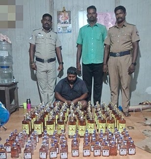   மதுப்புட்டிகளுடன் கைதான சந்தோஷ்குமாா். உடன் போலீஸாா். 