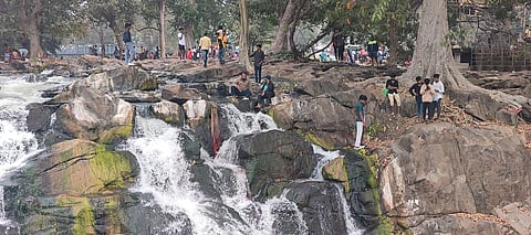 ஒகேனக்கல் பிரதான அருவி அருகில் வழுவழுப்பான பாறையின் மீது ஏறி புகைப்படம் எடுக்கும் சுற்றுலாப் பயணிகள்