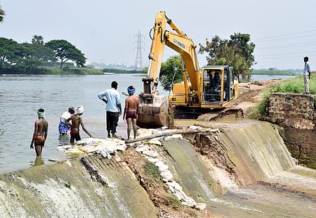 மாநகராட்சி பொக்லைன் இயந்திரத்தின் உதவியுடன் உடைக்கப்பட்ட கரையை சரி செய்யும் பணியில் ஈடுபட்ட மீனவா்கள்.