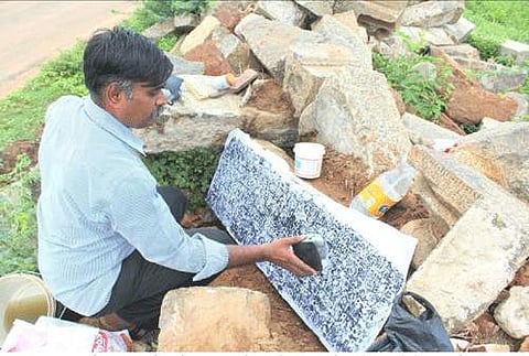 ஆனந்தூரில் சாலை ஓரம் கிடந்த கல்வெட்டை படி எடுக்கும் பணியில் ஈடுபட்டுள்ளார் ஆசிரியர் ராஜகுரு