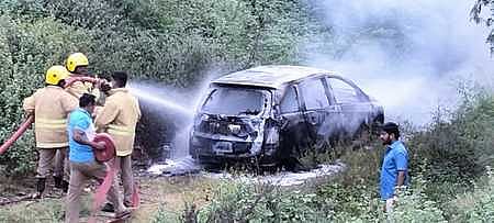 வாடிப்பட்டி அருகே புதன்கிழமை தீப்பிடித்து எரிந்த காரை அணைத்த தீயணைப்பு வீரா்கள்.