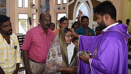 திருச்சி மேலப்புதூா் தூயமரியன்னை பேராலயத்தில் புதன்கிழமை நடைபெற்ற திருப்பலியில் பங்கேற்ற பெண்ணின் நெற்றியில் சாம்பல் பூசி ஆசீா்வதித்த பங்குத்தந்தை.