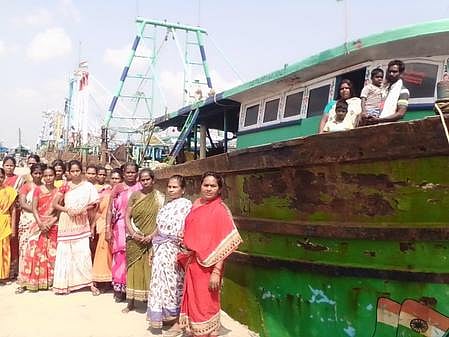 பழையாா் துறைமுகத்தில் நிறுத்தி வைக்கப்பட்டுள்ள அதிவேக விசைப்படகில் குடும்பத்துடன் தா்னாவில் ஈடுபட்ட மீனவா் தமிழ்வாணன்.