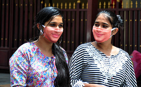 தங்களின் முகத்தைப் போன்றே இருக்கும் புது வித முகக் கவசம் அணிந்துள்ள கோவை இளம்பெண்கள்.