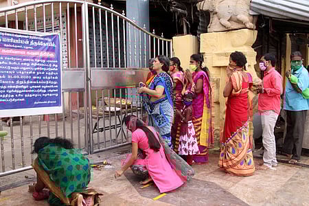 கரோனா பொதுமுடக்கம் காரணமாக மூடப்பட்டுள்ள மதுரை தெப்பகுளம் மாரியம்மன் கோயில் வாசல் முன் நின்று வெள்ளிக்கிழமை சுவாமி தரிசனம் செய்யும் பக்தா்கள்.