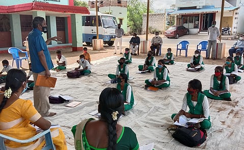 போடி அருகே டொம்புச்சேரியில் மரத்தடியில் மாணவா்களுக்கு பாடம் நடத்திய ஆசிரியா்கள்.